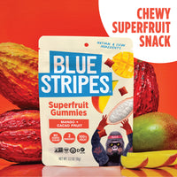 Blue Stripes Mango Superfruit Gummies pouch displayed in front of whole cacao pods and mangos on a red background.
