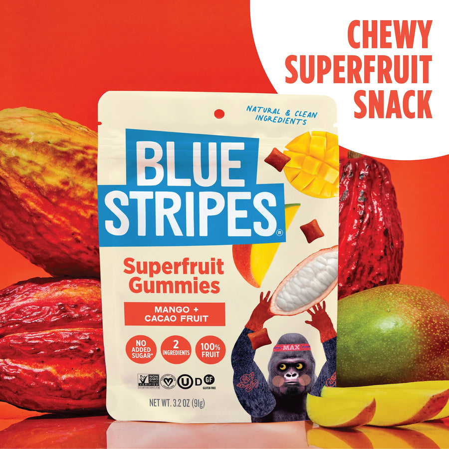 Blue Stripes Mango Superfruit Gummies pouch displayed in front of whole cacao pods and mangos on a red background.